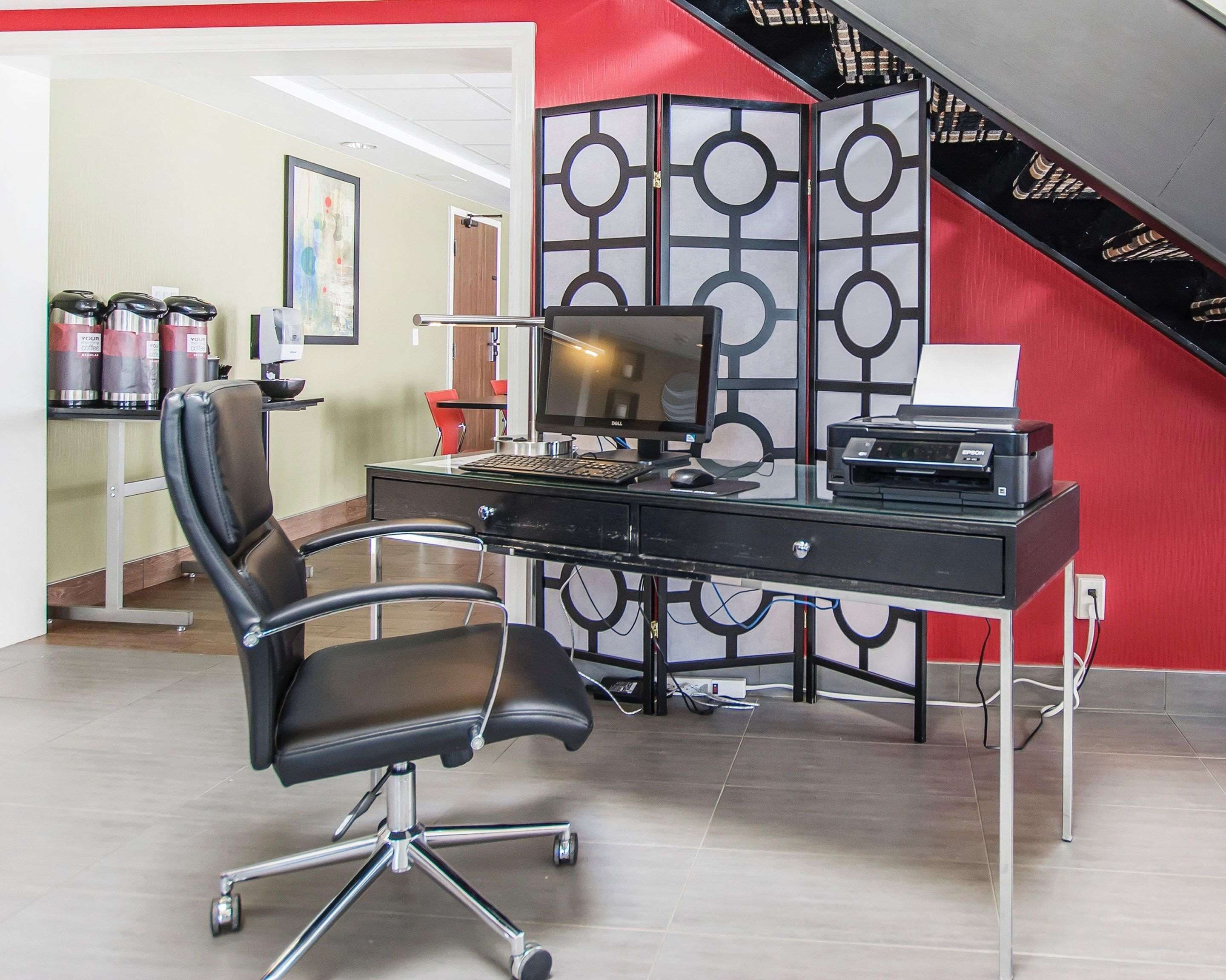 A modern office space with a black desk, a swivel chair, a desktop computer, and a printer.