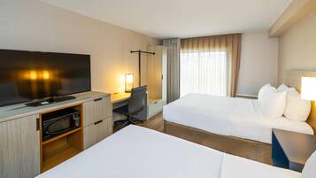 A hotel room with a flat-screen TV, a desk with a chair, a bed, and a window with curtains.