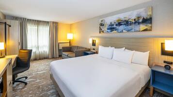 A hotel room with a large bed, a desk, a chair, a nightstand, and a painting on the wall.