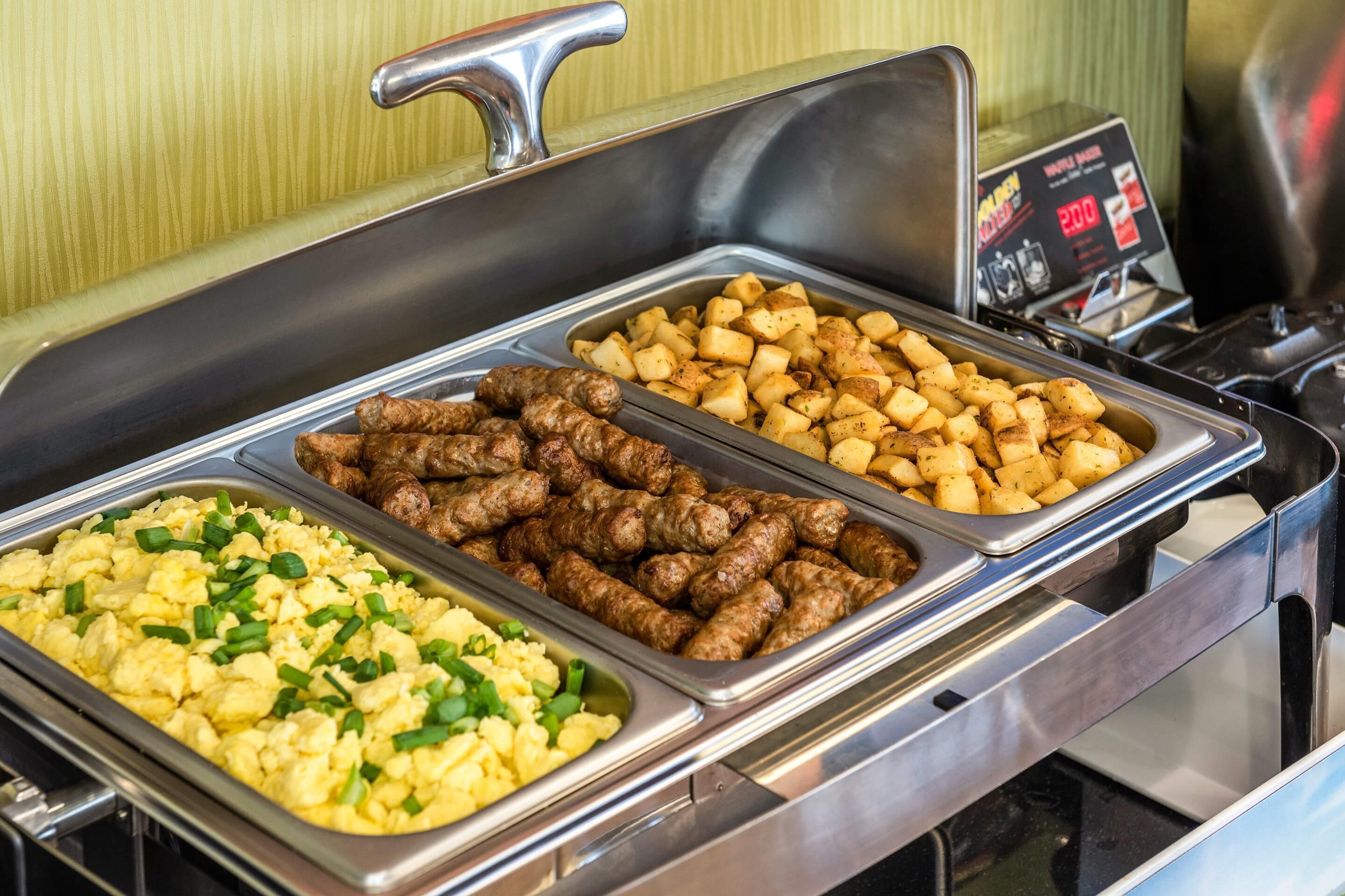Un buffet proposant trois plats différents : des œufs brouillés, des boulettes de viande et des pommes de terre rôties.