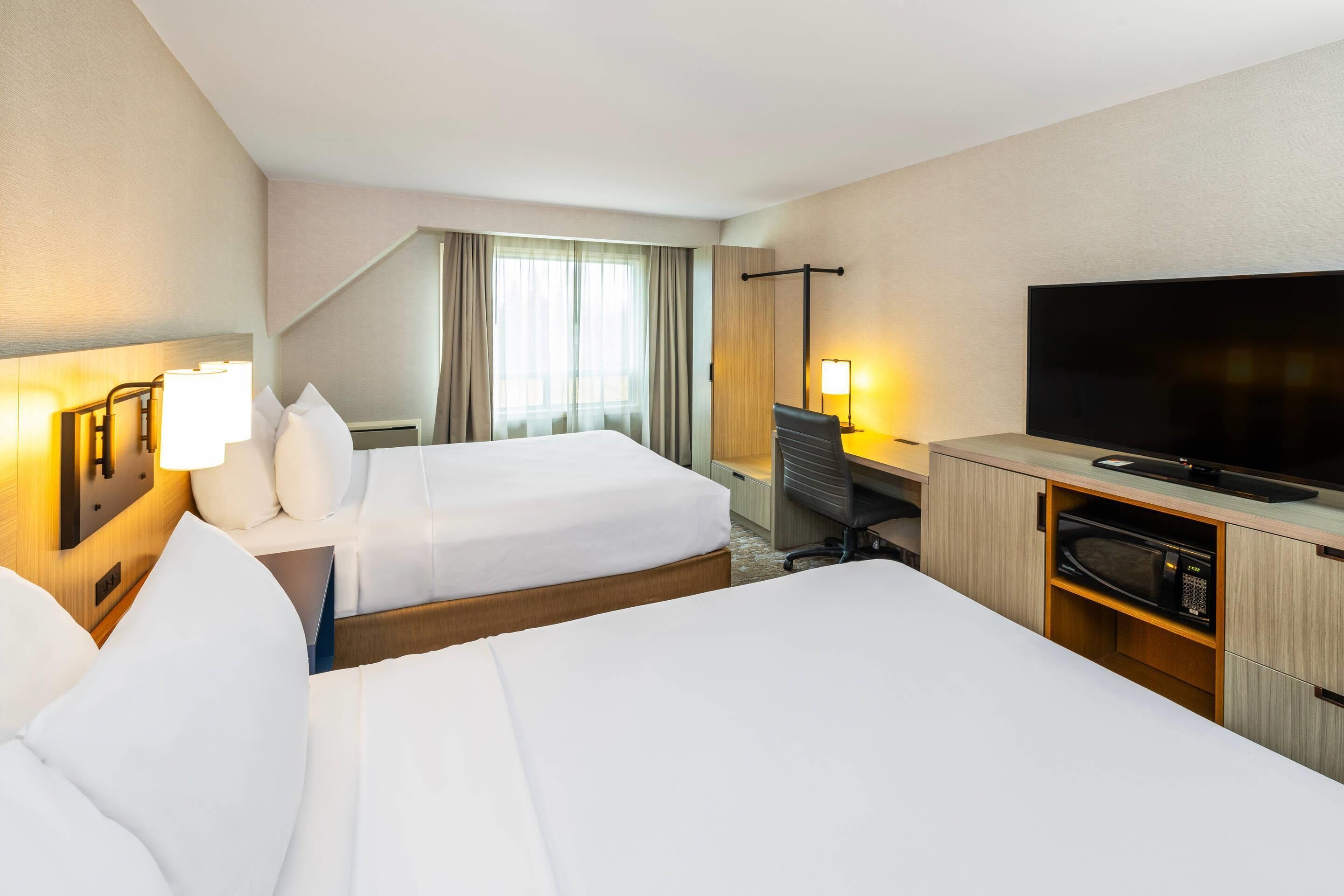 A hotel room with two beds, a desk with a computer, a TV, and a microwave.