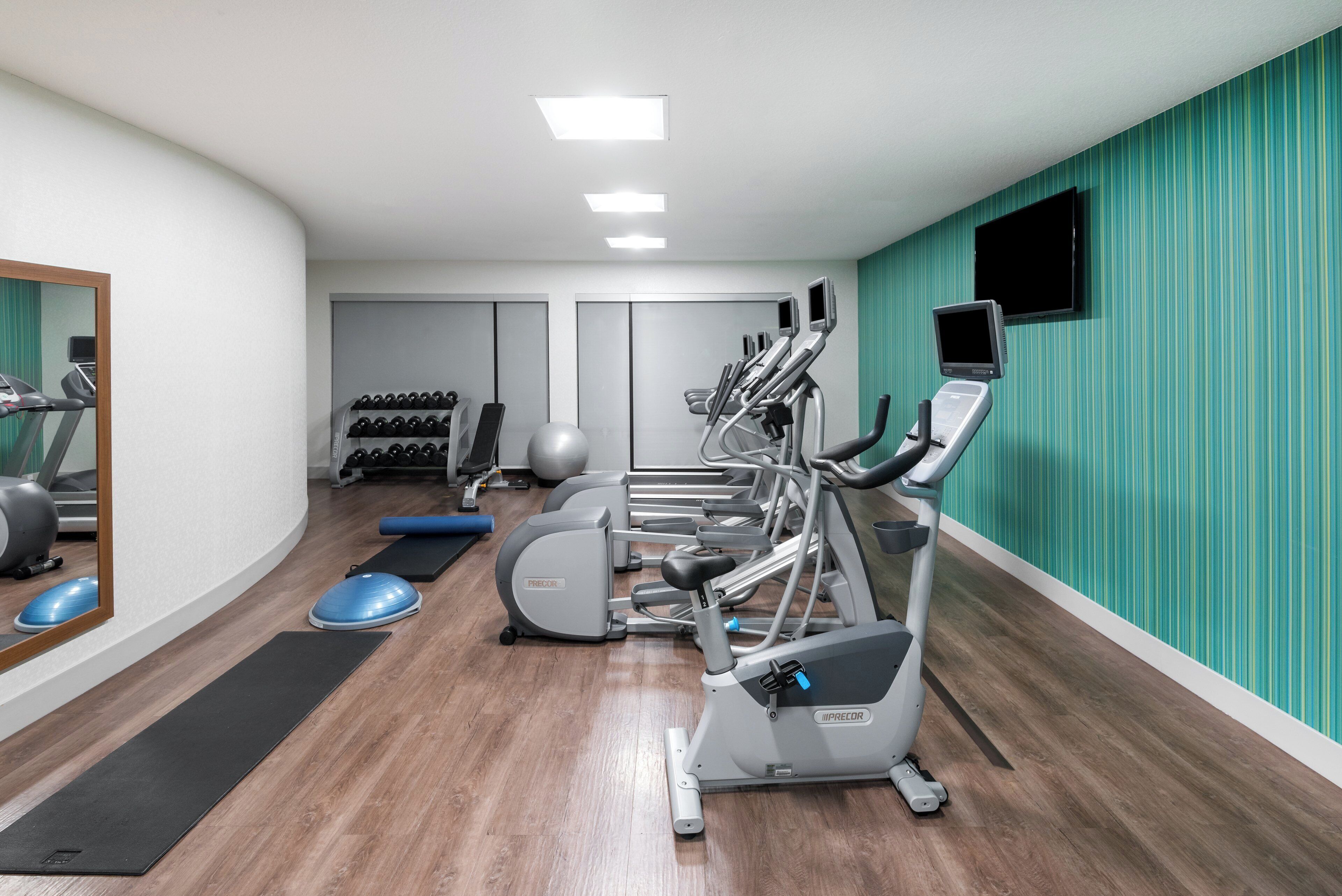 A gym with exercise equipment, a mirror, and a teal wall.