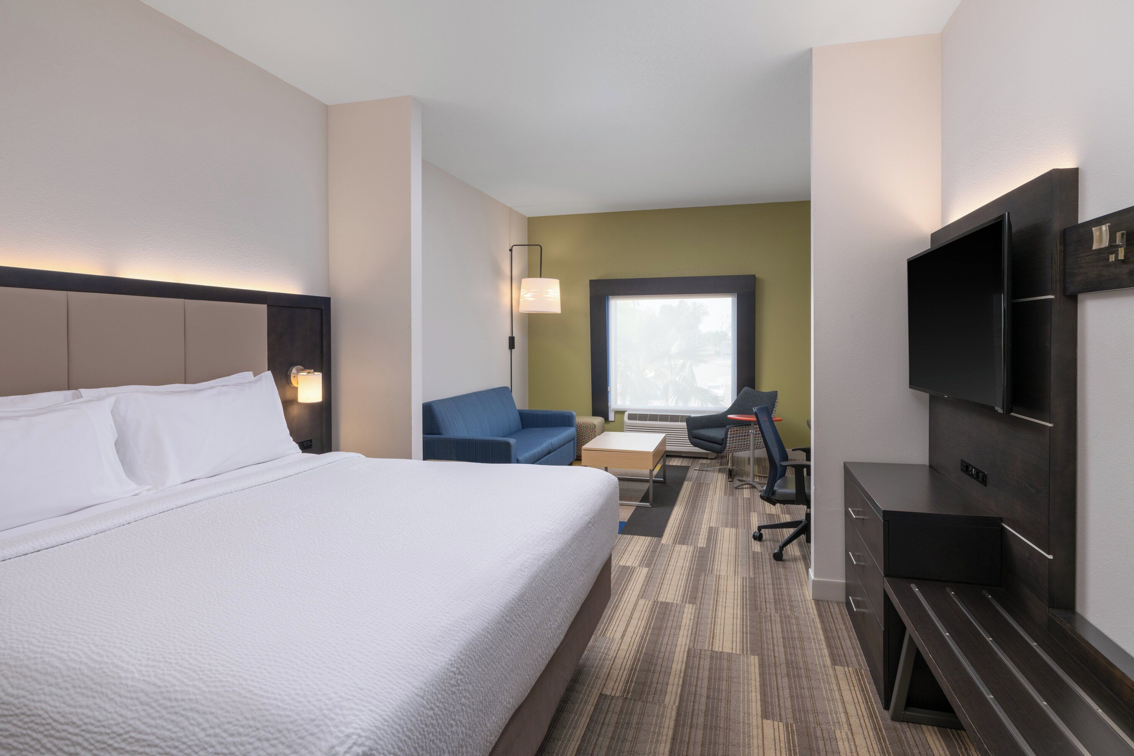 A hotel room with a large bed, a desk with a chair, a sofa, and a TV mounted on the wall.