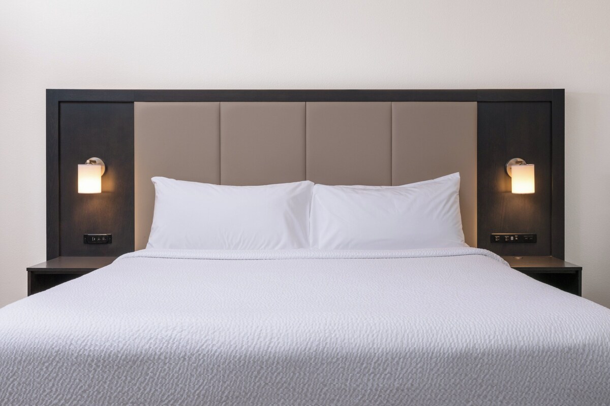 A neatly made bed with a padded headboard and two wall-mounted nightstands with integrated lighting.