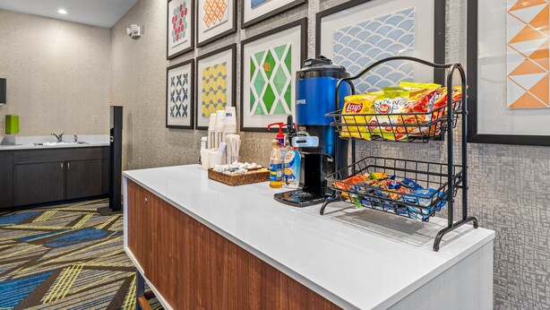 A hotel reception area with a coffee station, snack bar, and framed artwork on the wall.