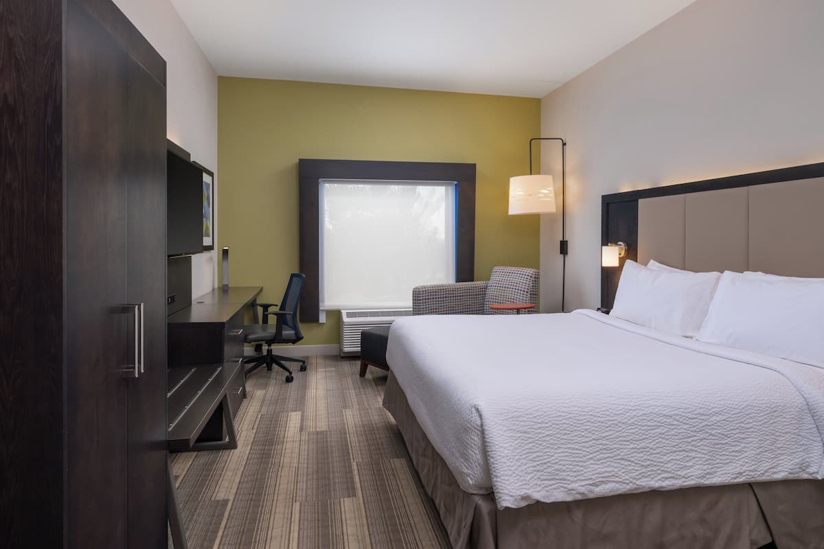 Hotelkamer met een groot bed, een bureau met stoel, een televisie en een raam met uitzicht op het omliggende landschap.