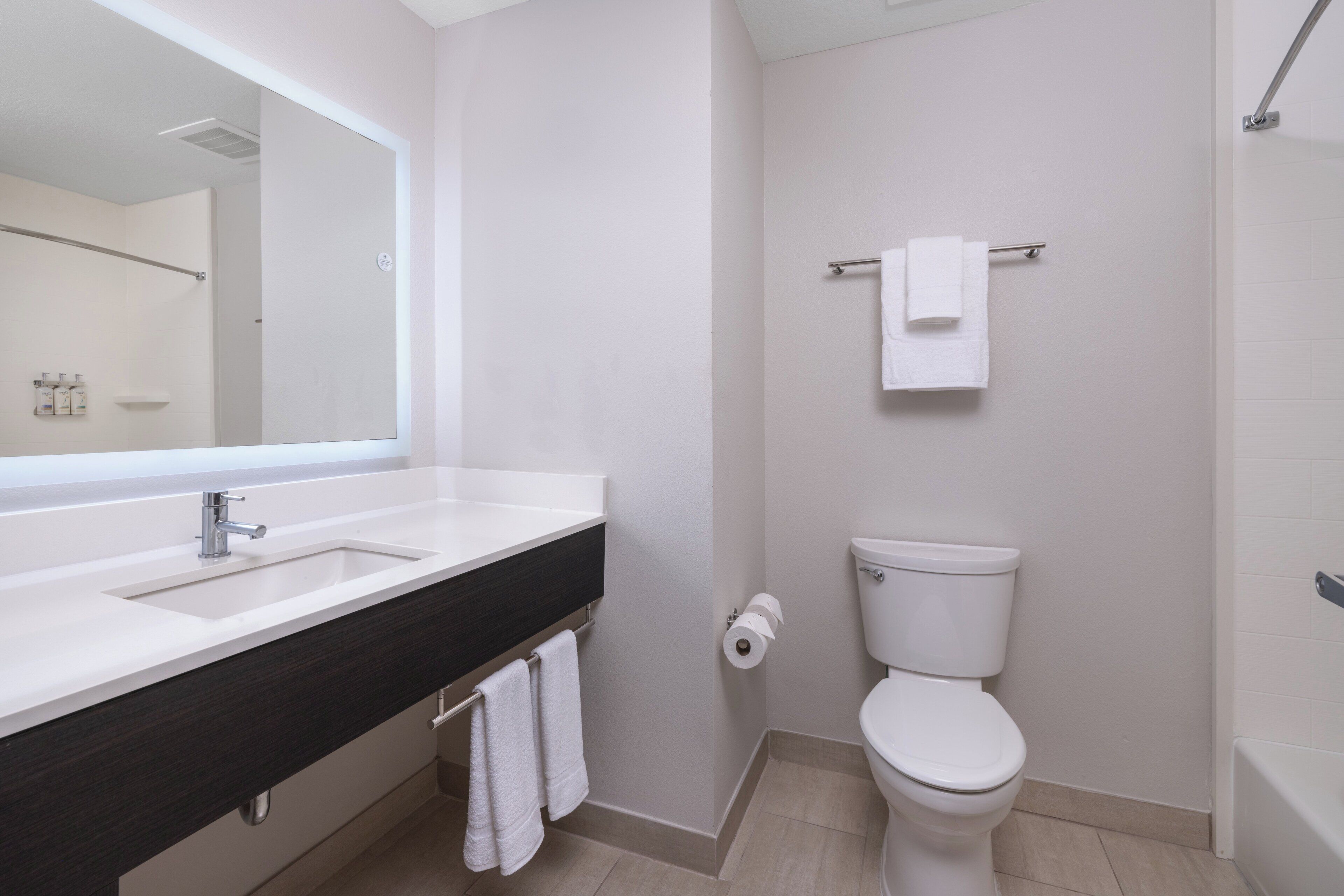 A modern bathroom with a large mirror, two sinks, a toilet, and a bathtub.