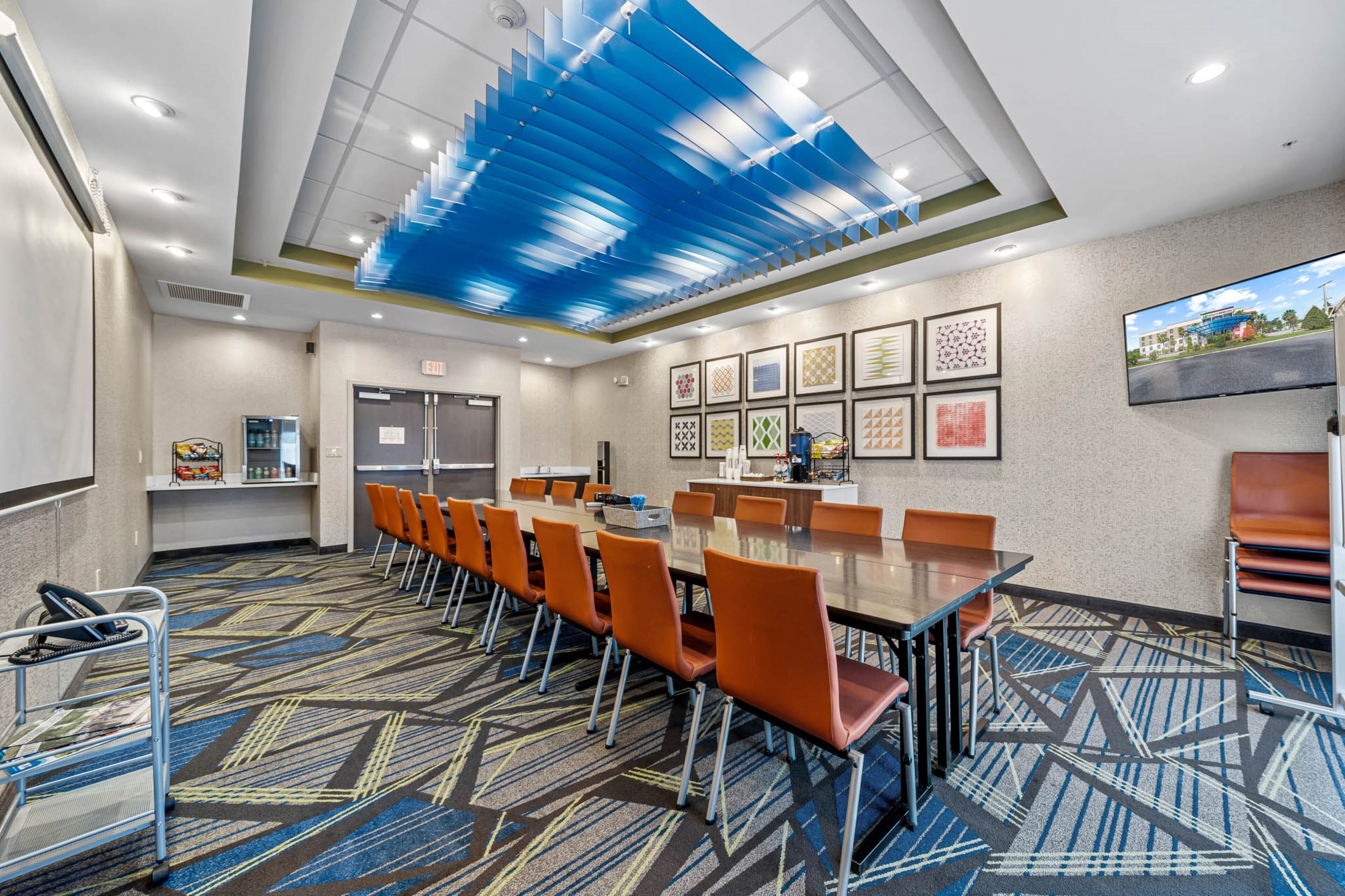 A conference room with a long table, orange chairs, a TV screen, and framed artwork on the wall.