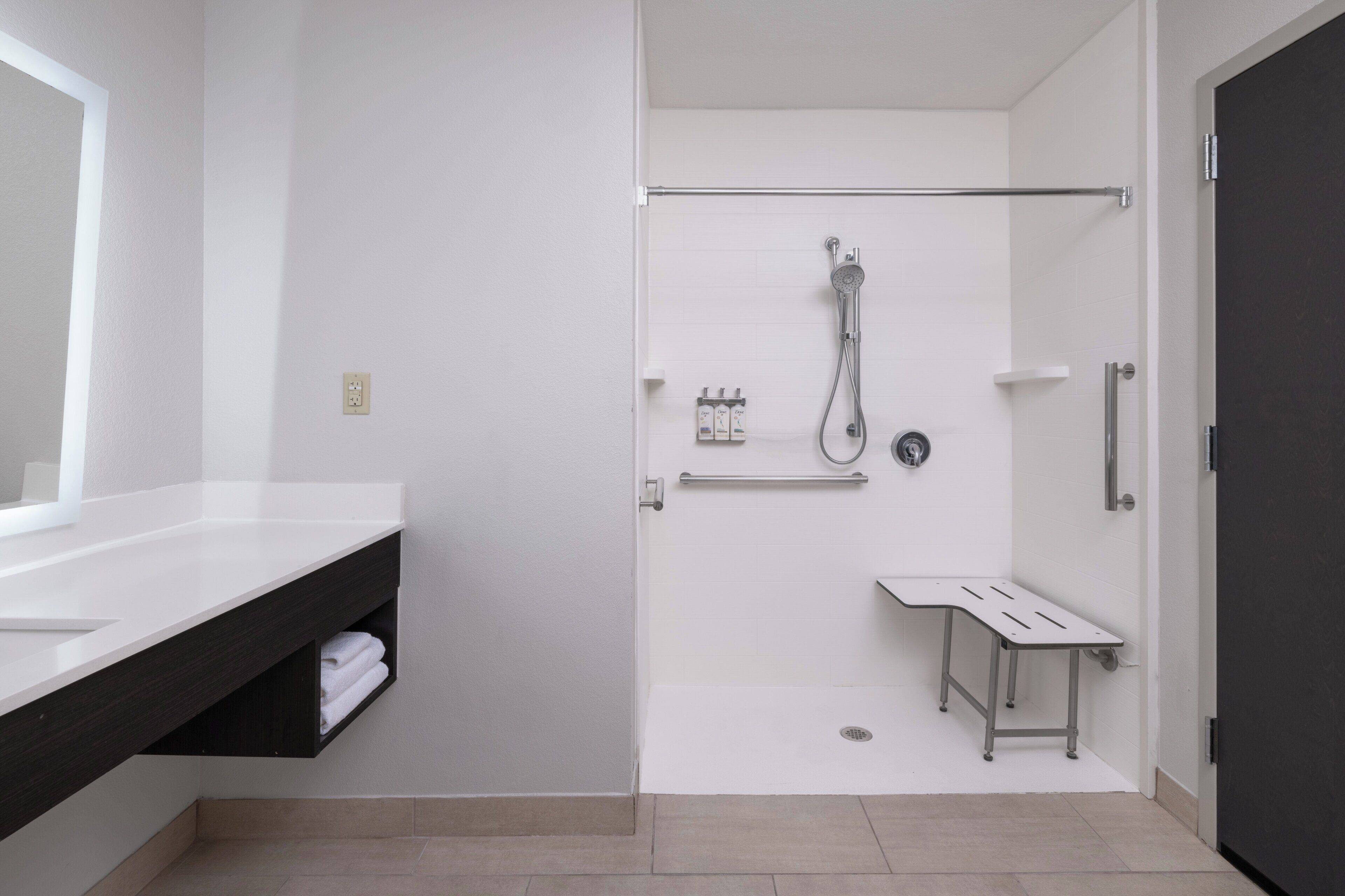 Een moderne badkamer met een wit wastafel, donker aanrecht, douche en een klein tafeltje.
