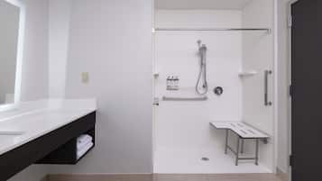 Een moderne badkamer met een wit wastafel, donker aanrecht, douche en een klein tafeltje.