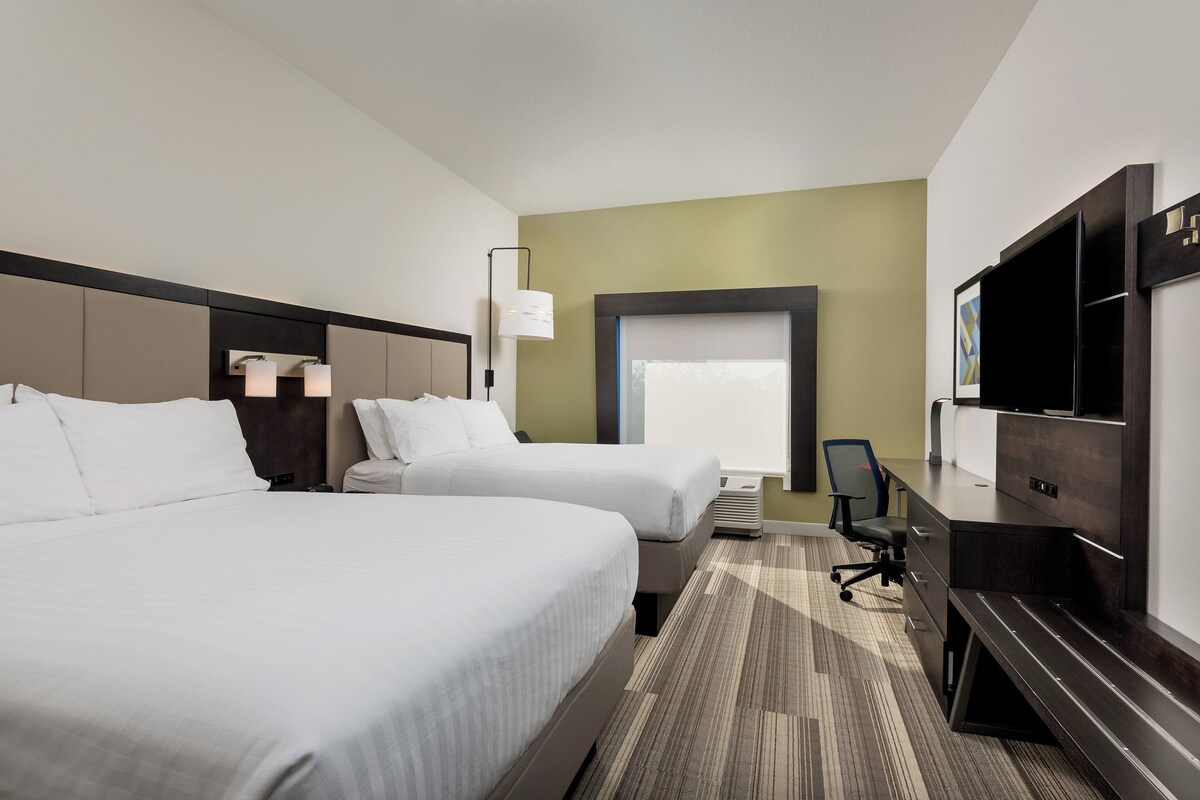 A hotel room with two beds, a desk, a chair, and a large window.