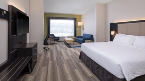 A hotel room with a large bed, a desk with a flat-screen TV, a sofa, and a window with a view of buildings.