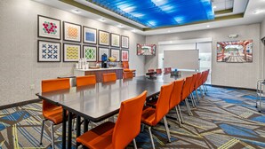 A conference room with a long table, orange chairs, framed artwork on the walls, and a patterned carpet.
