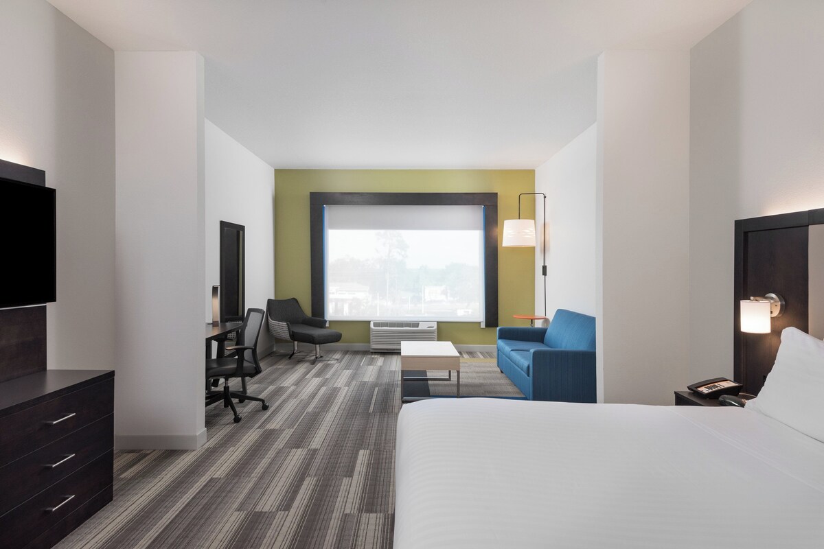 A hotel room with a bed, a desk, a chair, a sofa, a TV, and a window with a view.