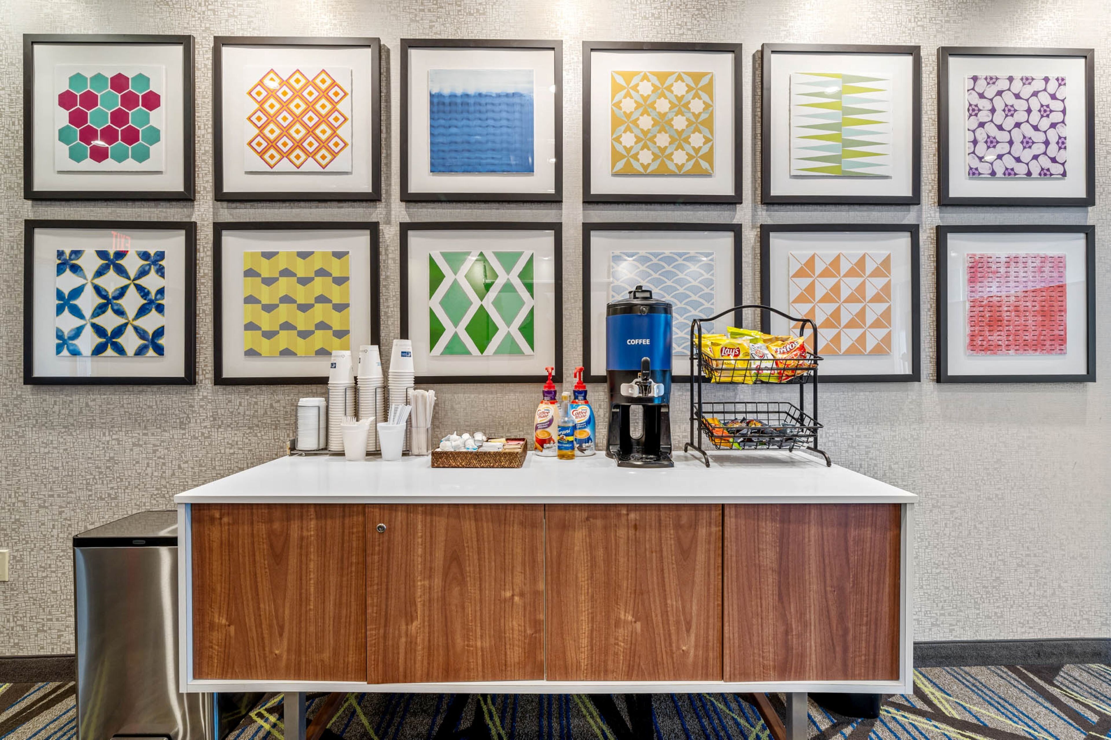 Ein Hotel-Empfangsbereich mit einer Holztresen, gerahmten Kunstwerken an der Wand und verschiedenen Annehmlichkeiten wie Kaffee, Snacks und Toilettenartikeln.