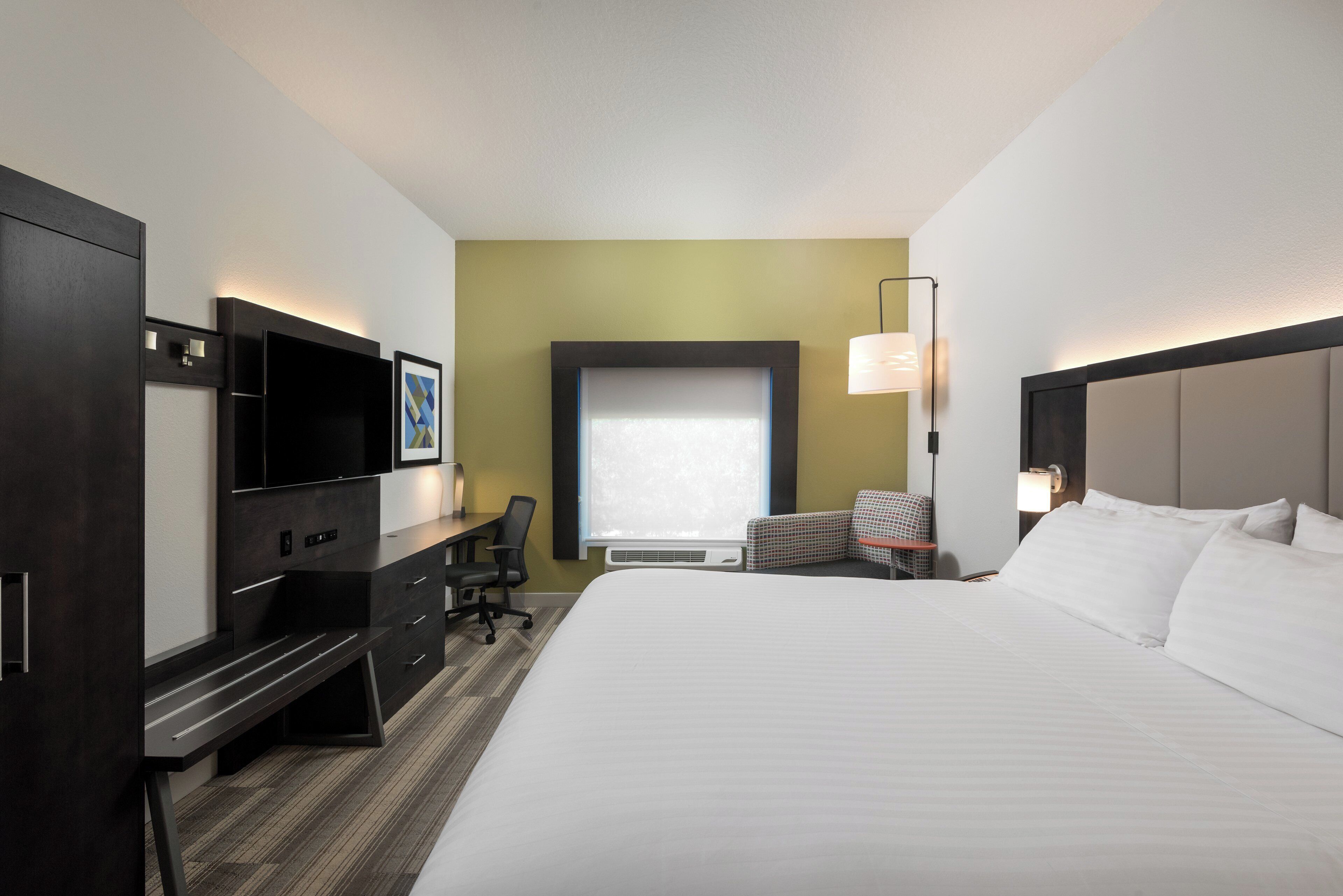 Habitación de hotel con cama, escritorio, silla, televisor y ventana.