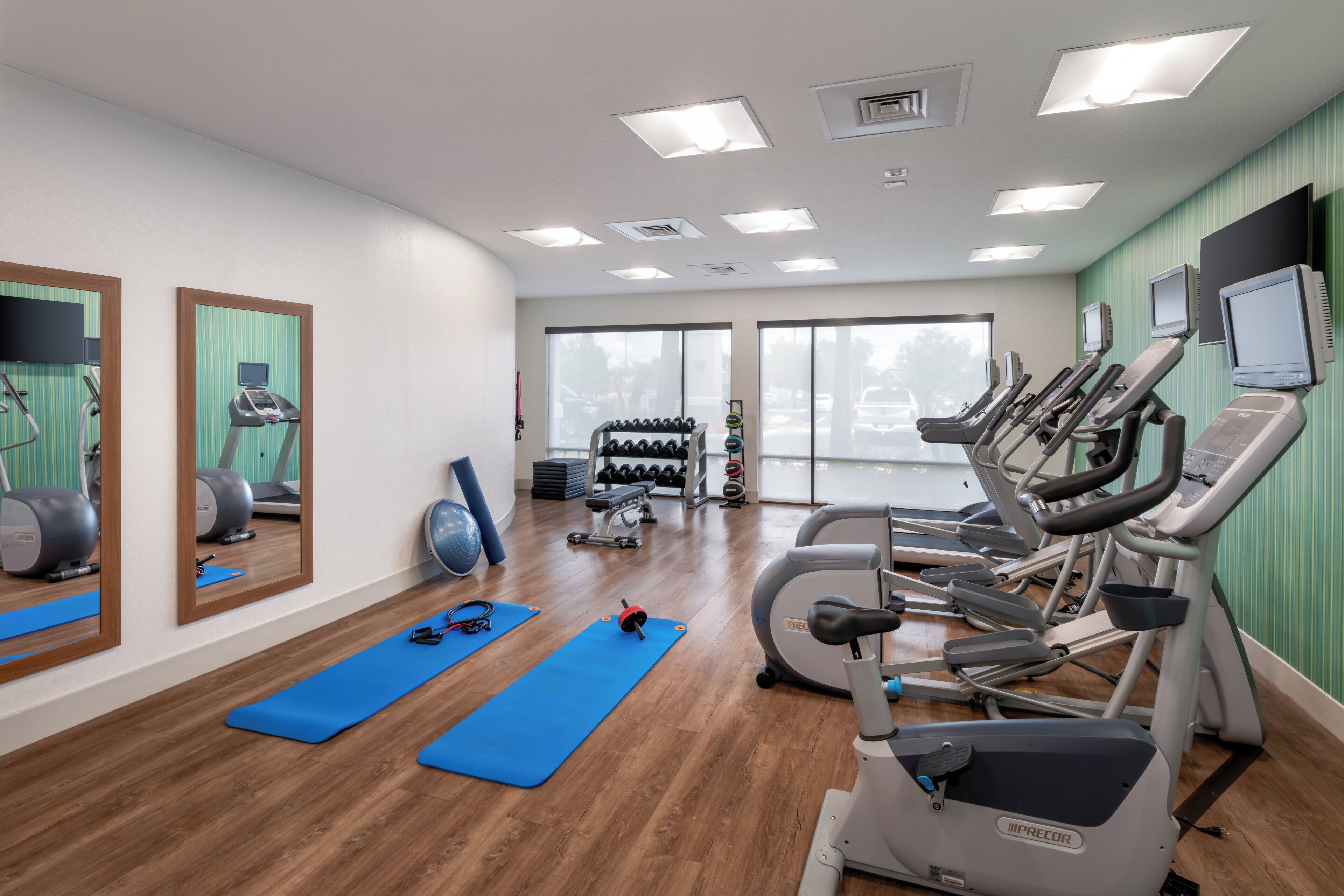 A gym with exercise equipment, blue mats, and a large window.