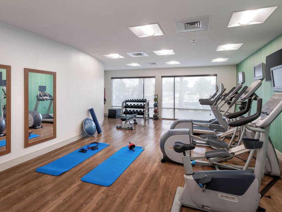 A gym with exercise equipment, blue mats, and a large window.