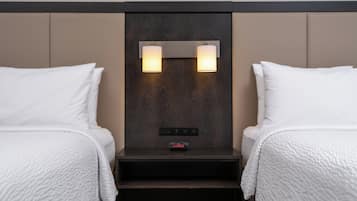 Habitación de hotel con dos camas, una mesita de noche con panel de control e iluminación en la pared.