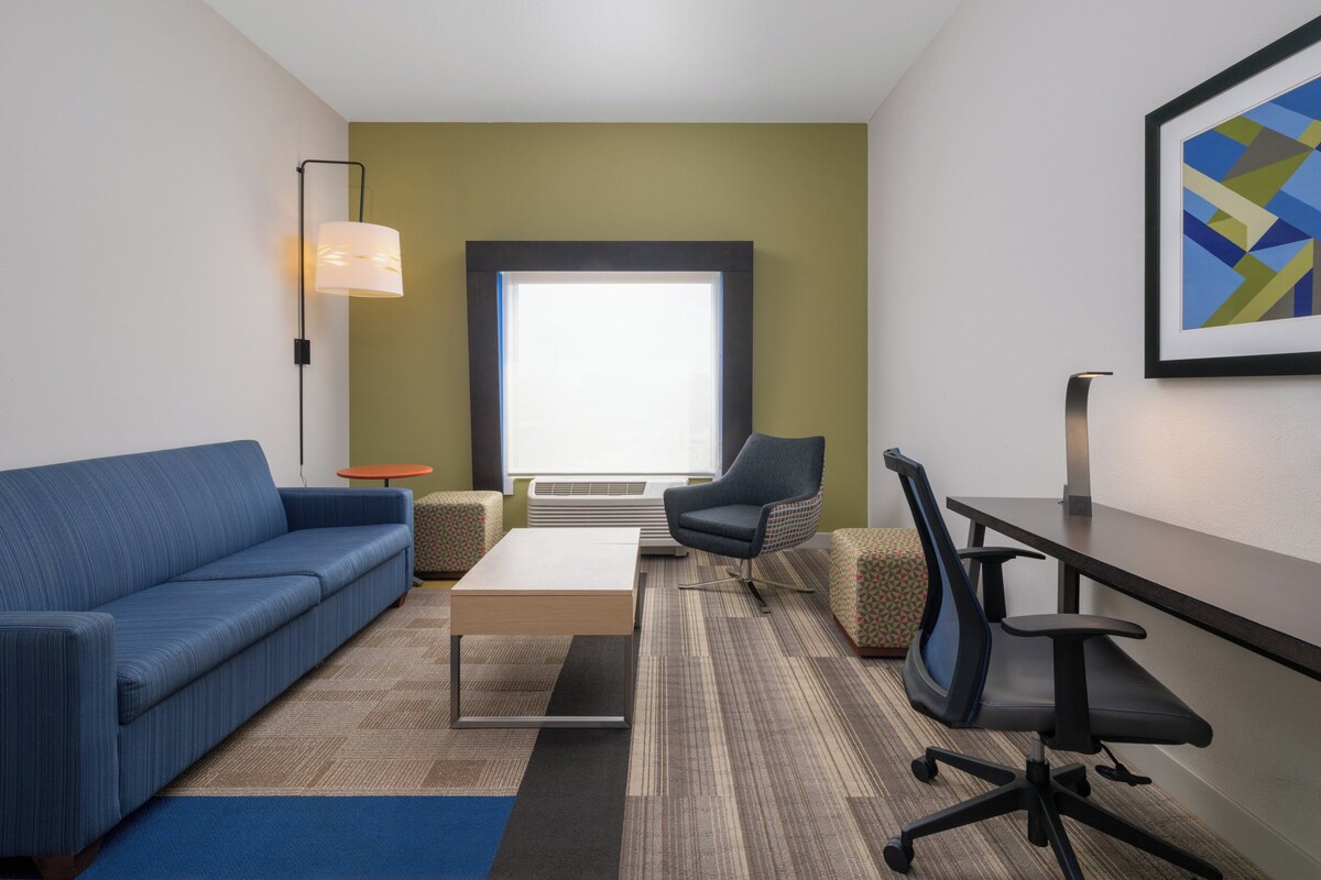 A modern hotel room with a blue sofa, a small round table, a large window, a chair, and a desk.
