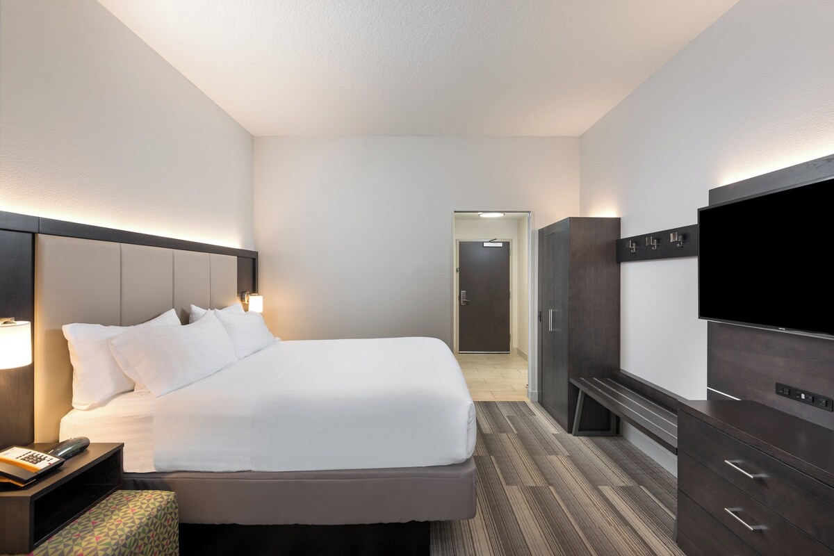 A hotel room with a bed, bedside table, lamp, TV, wardrobe, and a mirror.