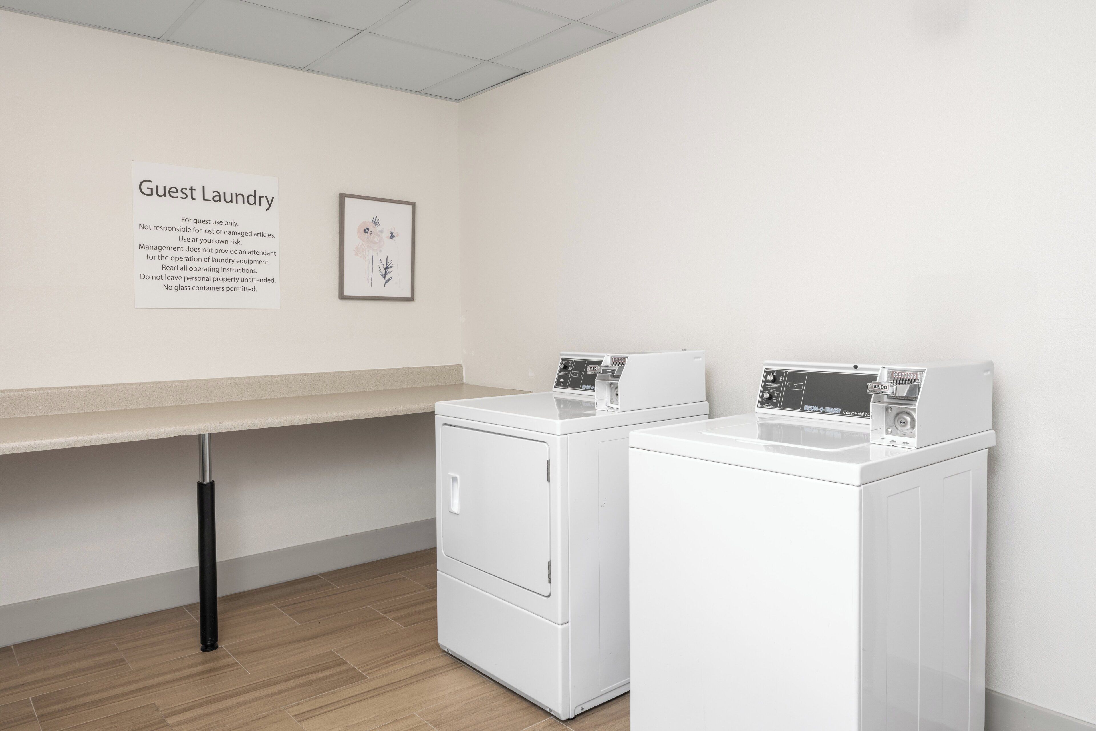 Un área de lavandería con dos lavadoras blancas, una encimera color beige y un cartel que dice 'Guest Laundry'.
