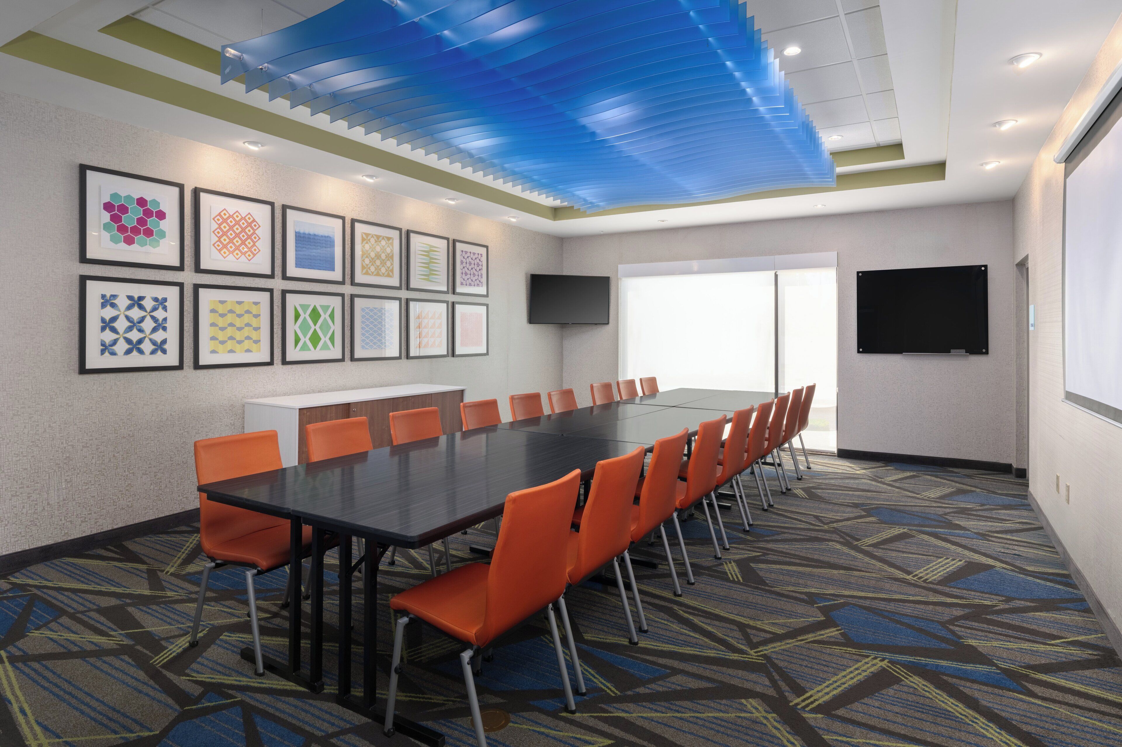 A conference room with a long table, orange chairs, framed artwork on the wall, and a blue ceiling.