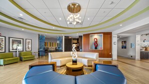 A modern lobby with a curved seating area, a central art piece, and a wooden reception desk.