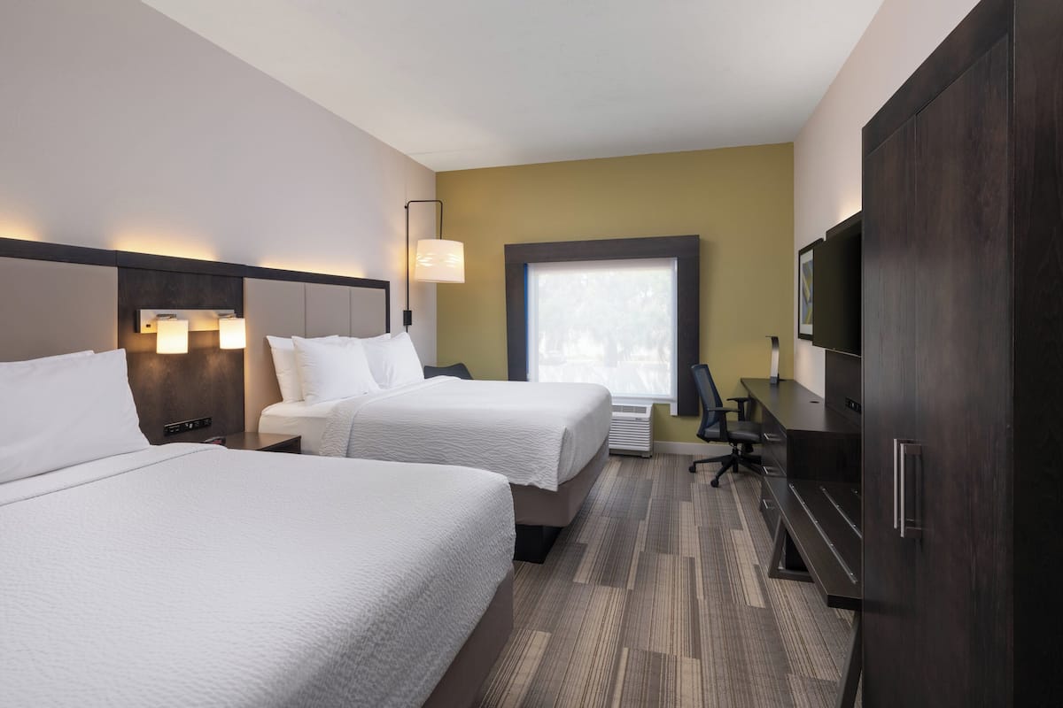 Een hotelkamer met twee bedden, een bureau, een stoel, een televisie en een raam met jaloezieën.