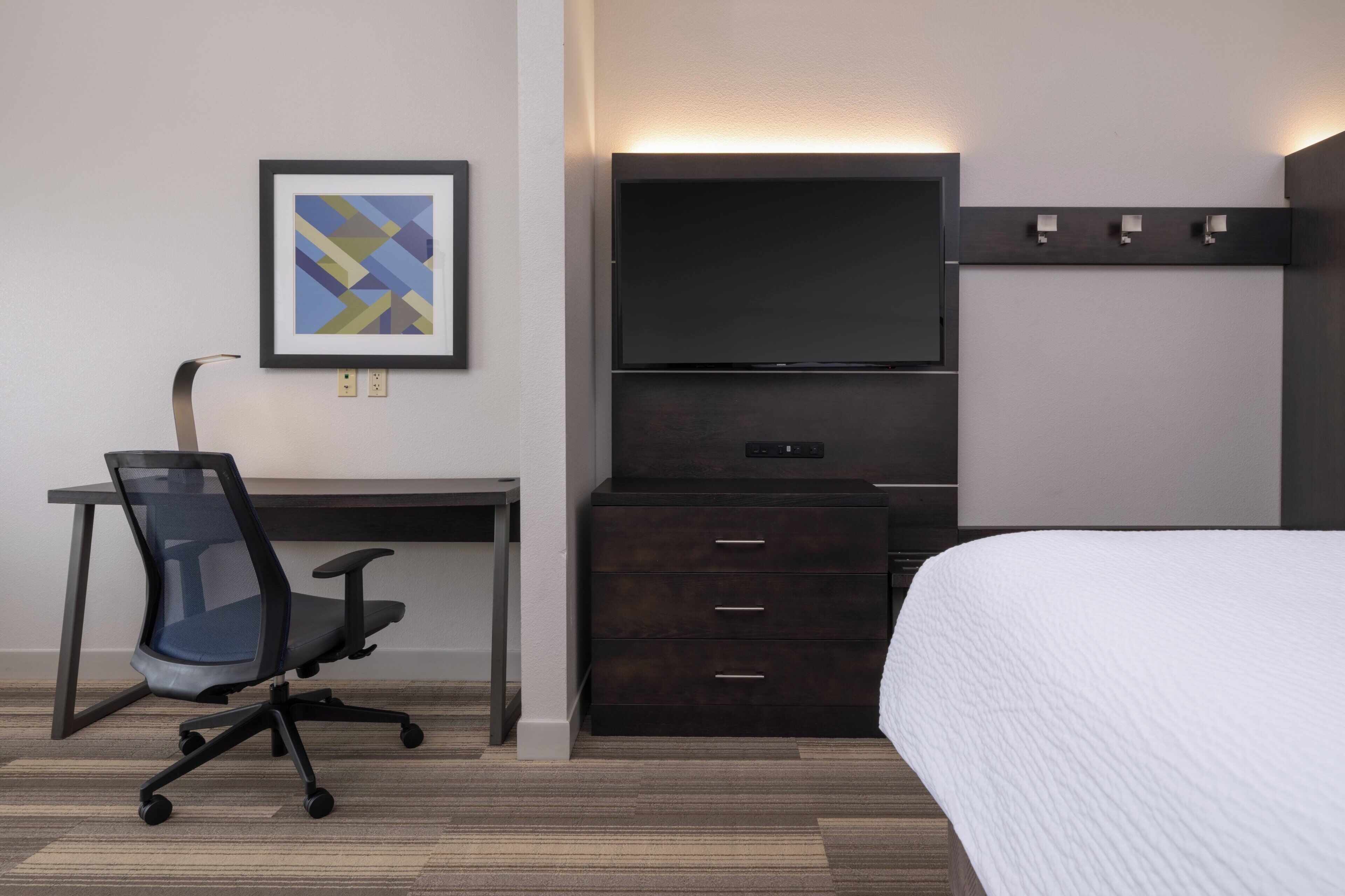 Habitación de hotel con cama, escritorio con silla, televisor de pantalla plana y cómoda.