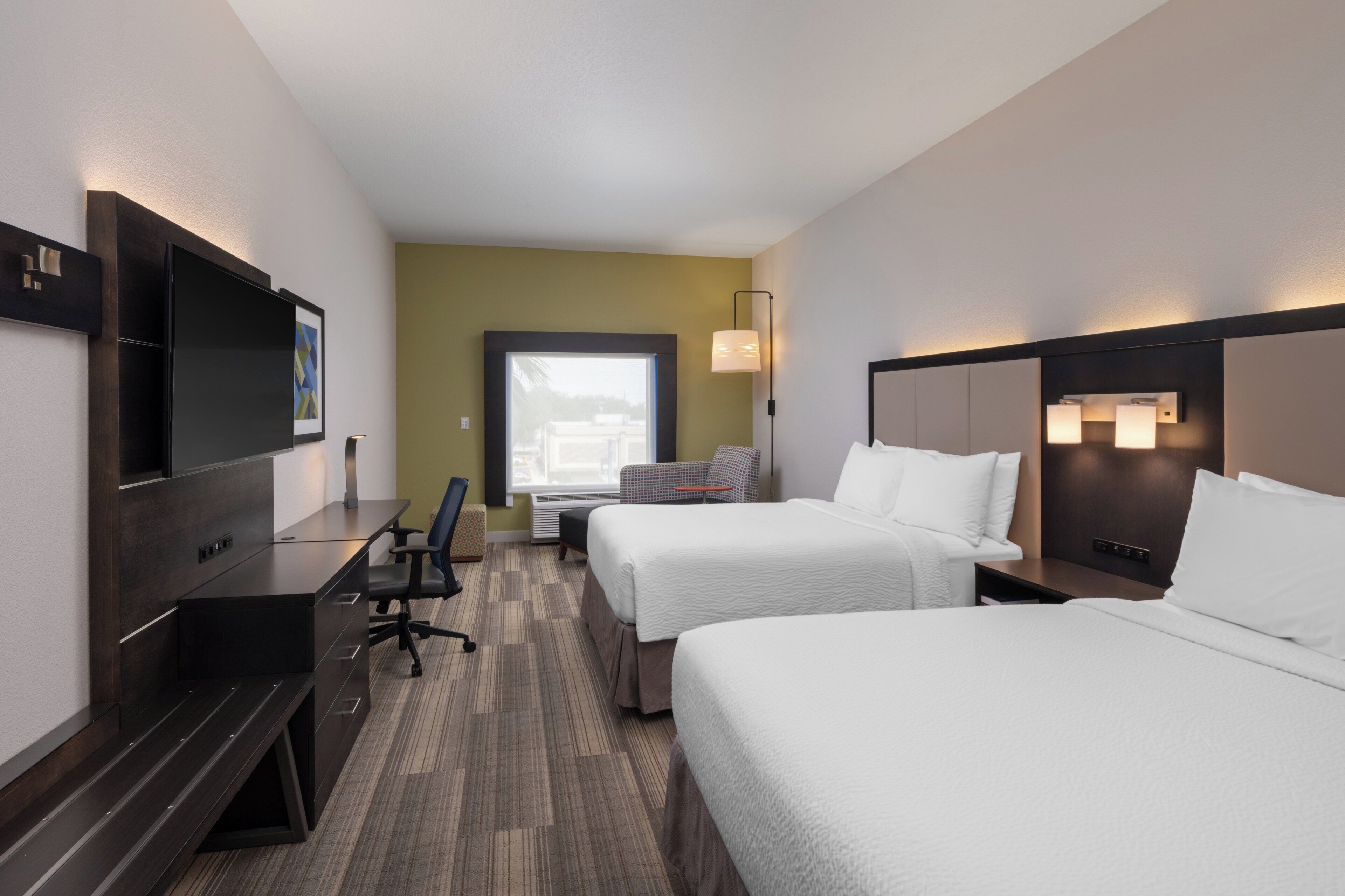 A hotel room with two beds, a desk, a chair, a TV, and a window.