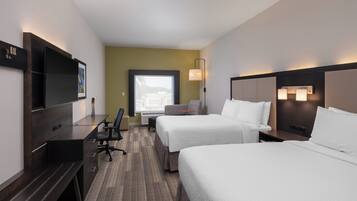 A hotel room with two beds, a desk, a chair, a TV, and a window.