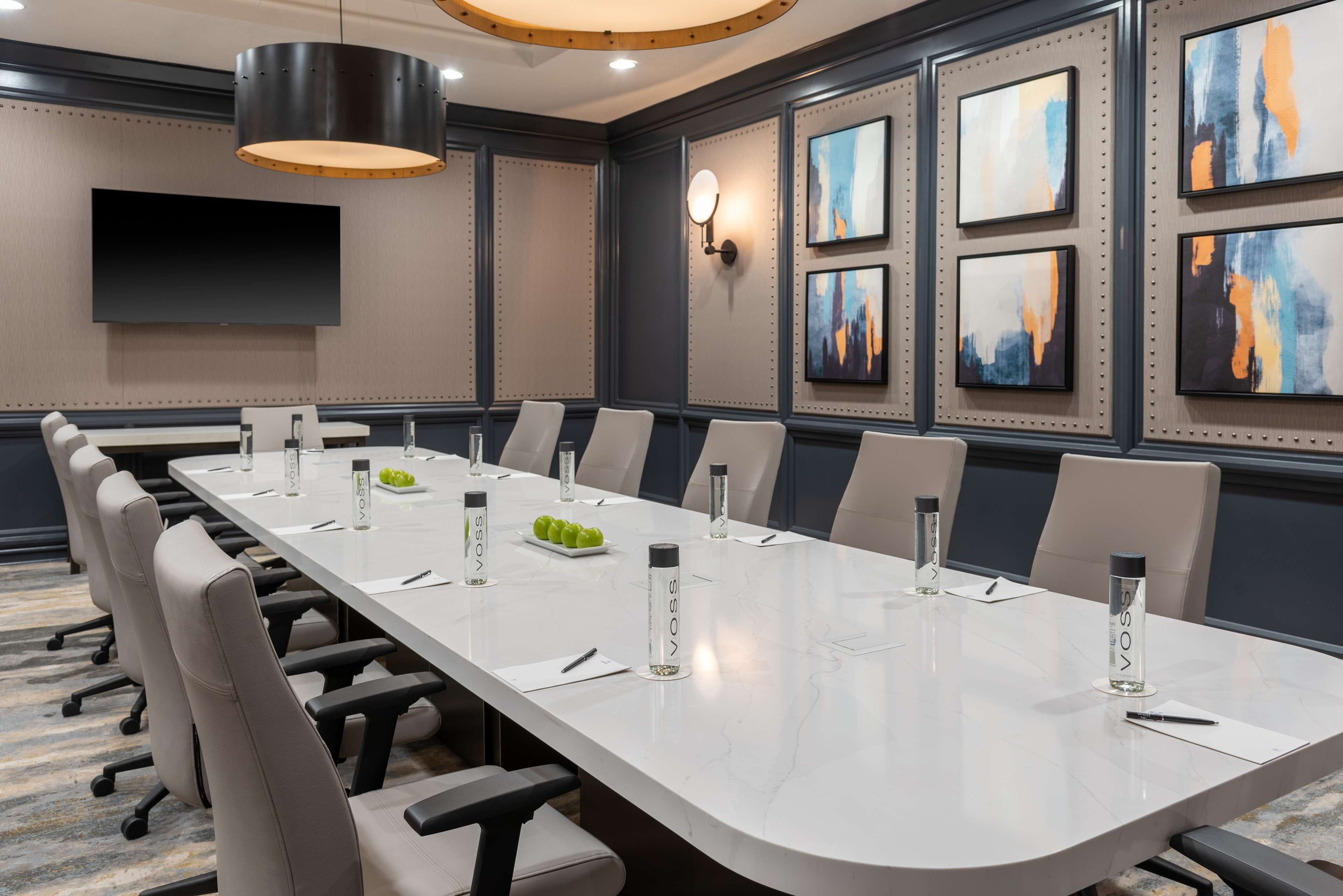 A conference room with a long table, chairs, water bottles, and a TV on the wall.