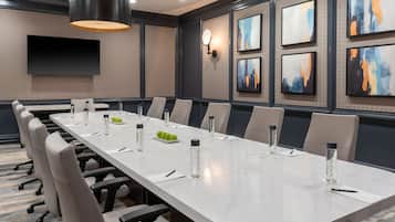 A conference room with a long table, chairs, water bottles, and a TV on the wall.