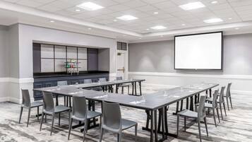 A conference room with a long table, chairs, a projector screen, and a kitchenette area.