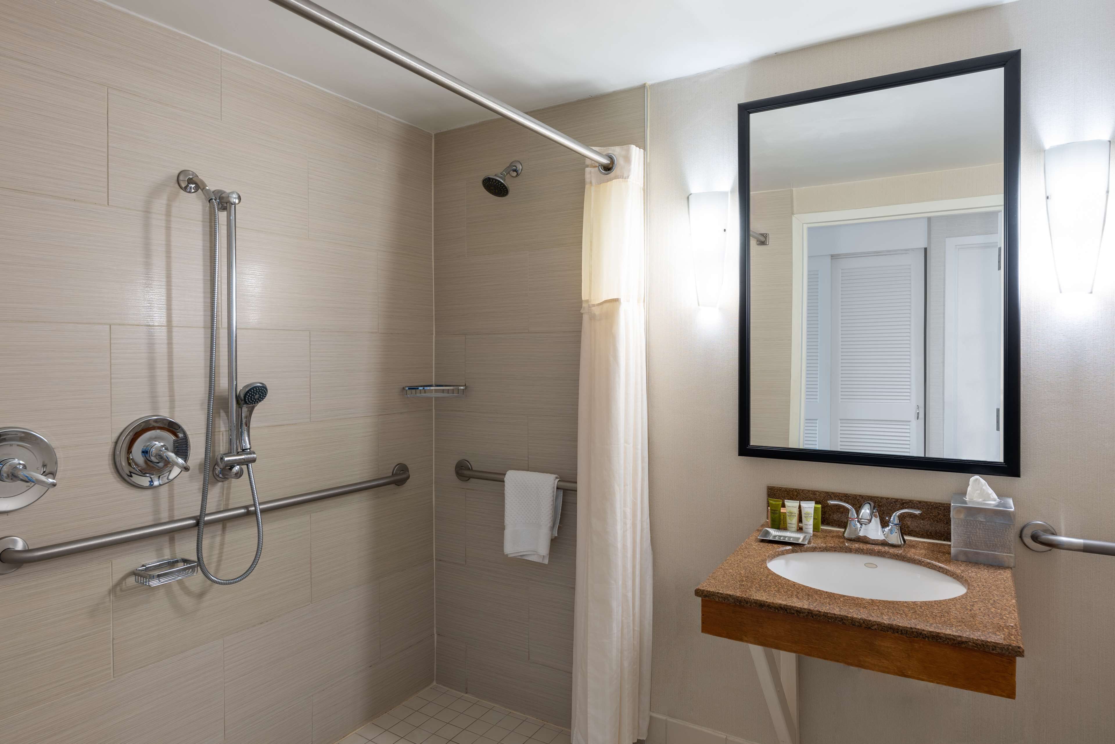 A bathroom with a shower, grab bars, a sink, and a mirror.