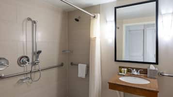 A bathroom with a shower, grab bars, a sink, and a mirror.