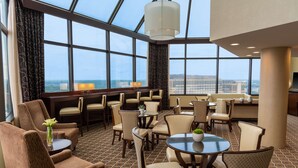 A hotel lobby with a high ceiling, large windows, and a seating area with tables and chairs. - Hilton Alexandria Mark Center (Alexandria)