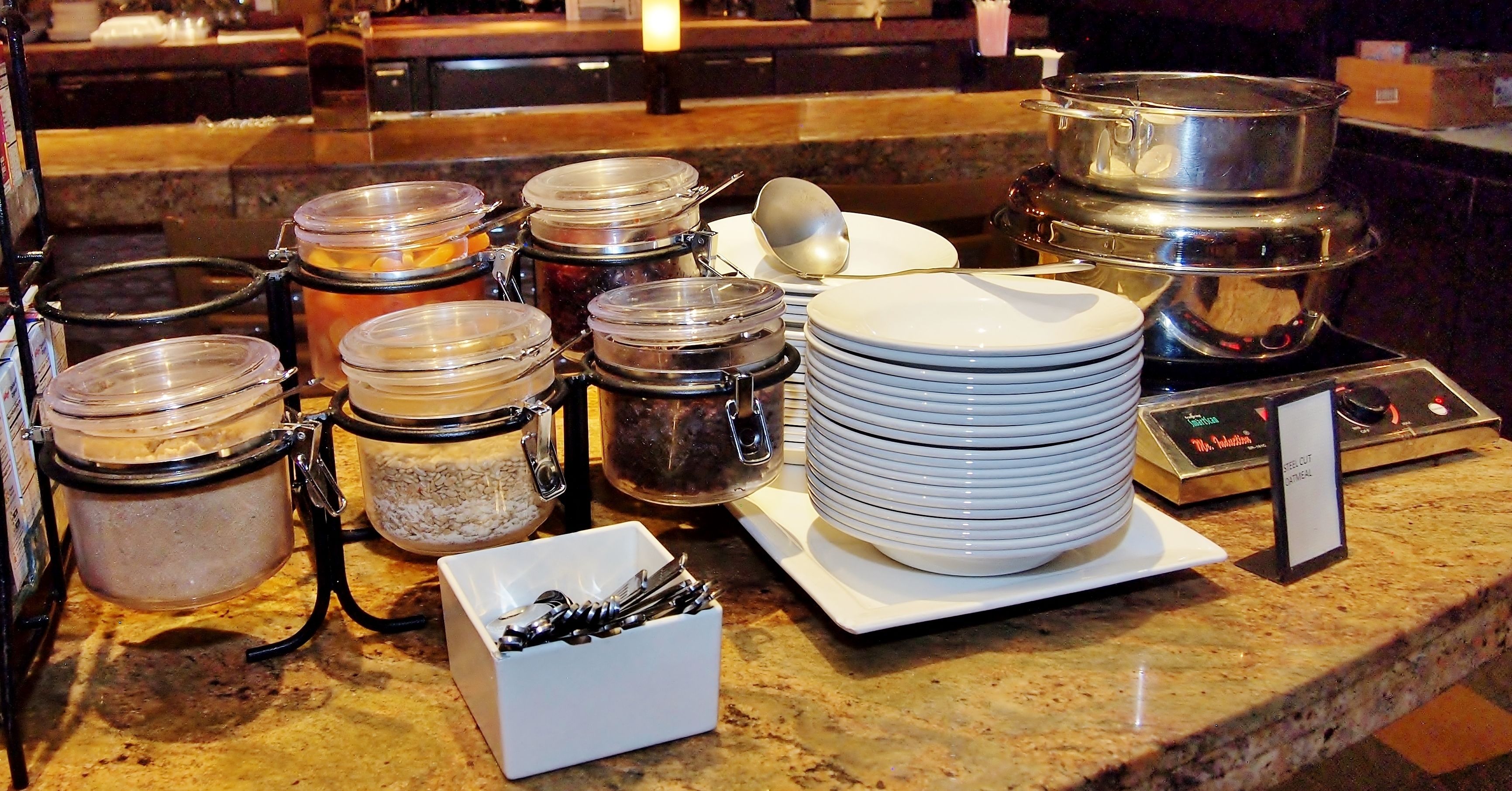 Montaje de bufé con diferentes recipientes de comida, platos y cubiertos.