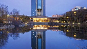 A high-rise hotel with a glass facade reflecting in a calm body of water. - Hilton Alexandria Mark Center (Alexandria)