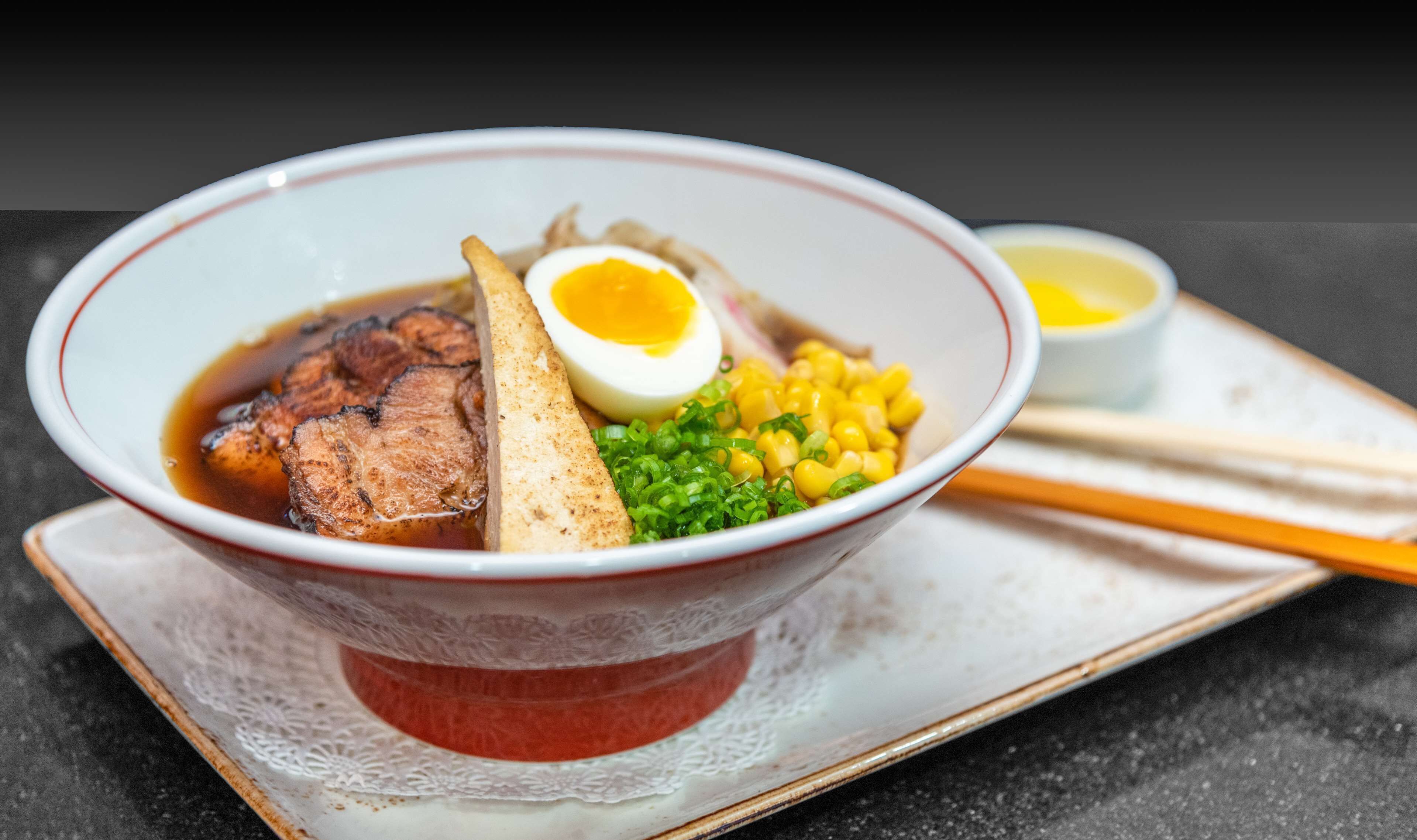 A bowl of ramen with meat, egg, corn, and green onions.