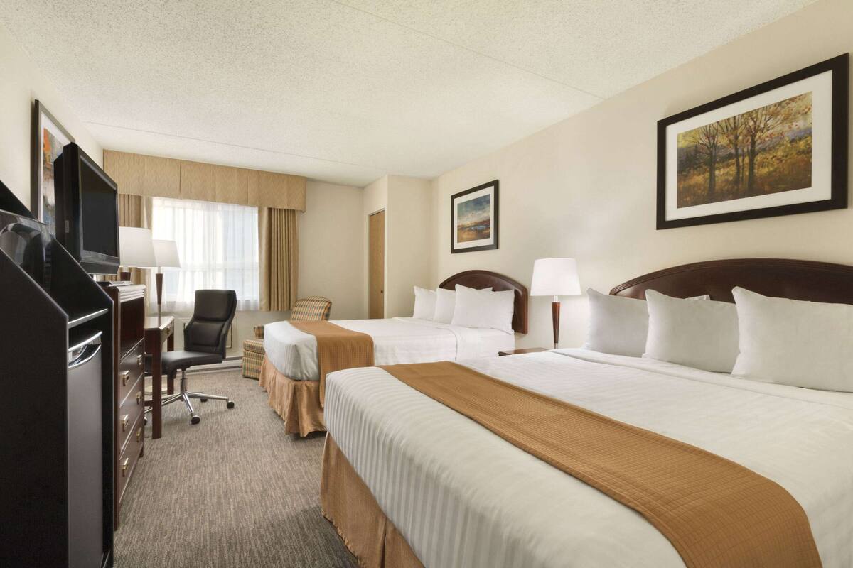 Een hotelkamer met twee bedden, een bureau met stoel, een televisie en een schilderij aan de muur.