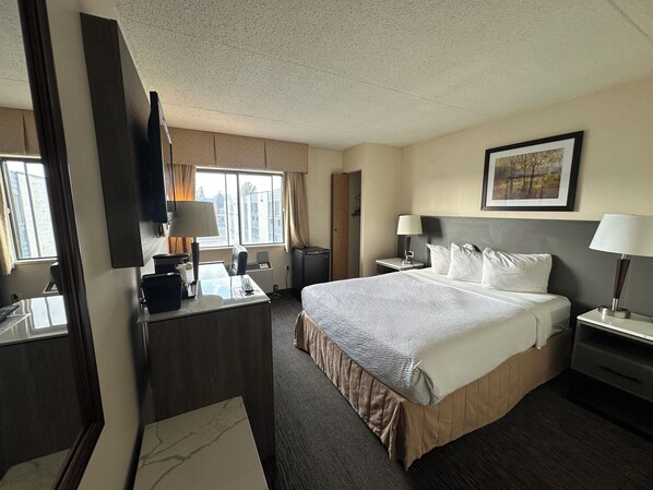 Habitación de hotel con una cama grande, un escritorio con computadora, una silla, un televisor y una ventana con cortinas.