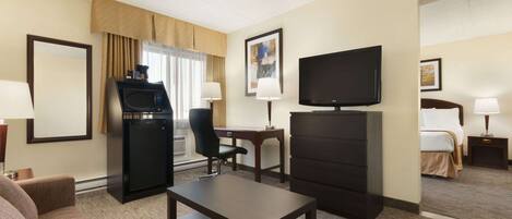 Habitación de hotel con sofá, una mesita, televisión, escritorio con silla, minibar y cama.