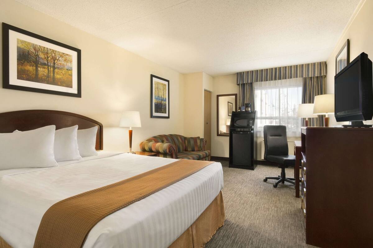 Een hotelkamer met een groot bed, een bureau, een televisie en een raam met gordijnen.