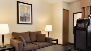 Une chambre d’hôtel avec un canapé marron, deux tables de chevet avec des lampes, un tableau encadré au mur, un four à micro-ondes et un réfrigérateur.