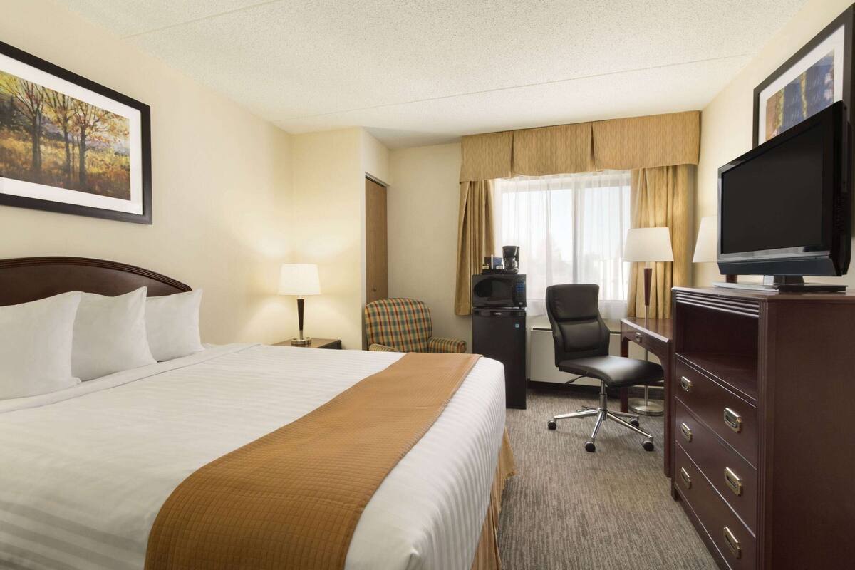 Een hotelkamer met een groot bed, een bureau met een televisie, een stoel en een dressoir.