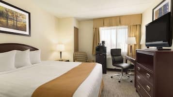 A hotel room with a large bed, a desk with a television, a chair, and a dresser.