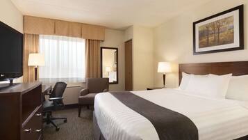 A hotel room with a large bed, a desk with a chair, a television, and a painting on the wall.