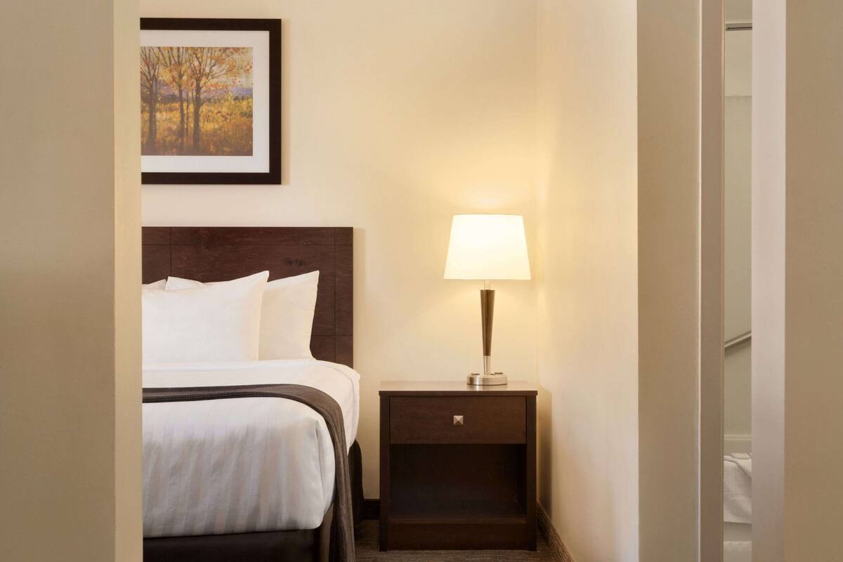 Een hotelkamer met een bed, een nachtkastje met een lamp en een ingelijst foto aan de muur.